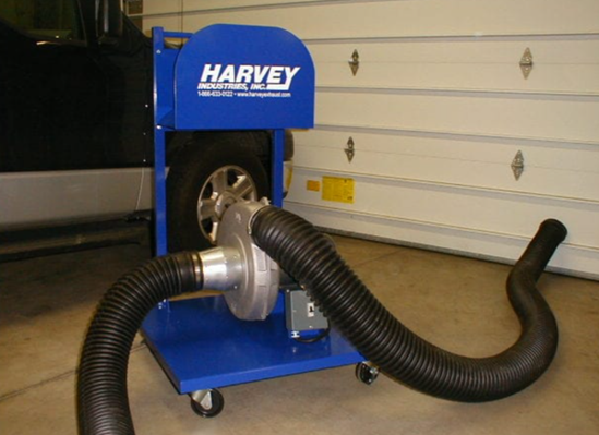 Blue Harvey tire balancing machine with a tire inside, featuring black hoses, in a garage.