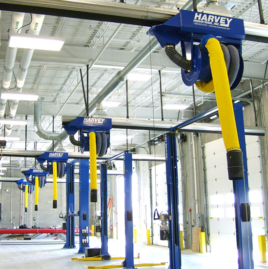 Blue and yellow Harvey exhaust systems suspended above car lifts in a brightly lit garage.