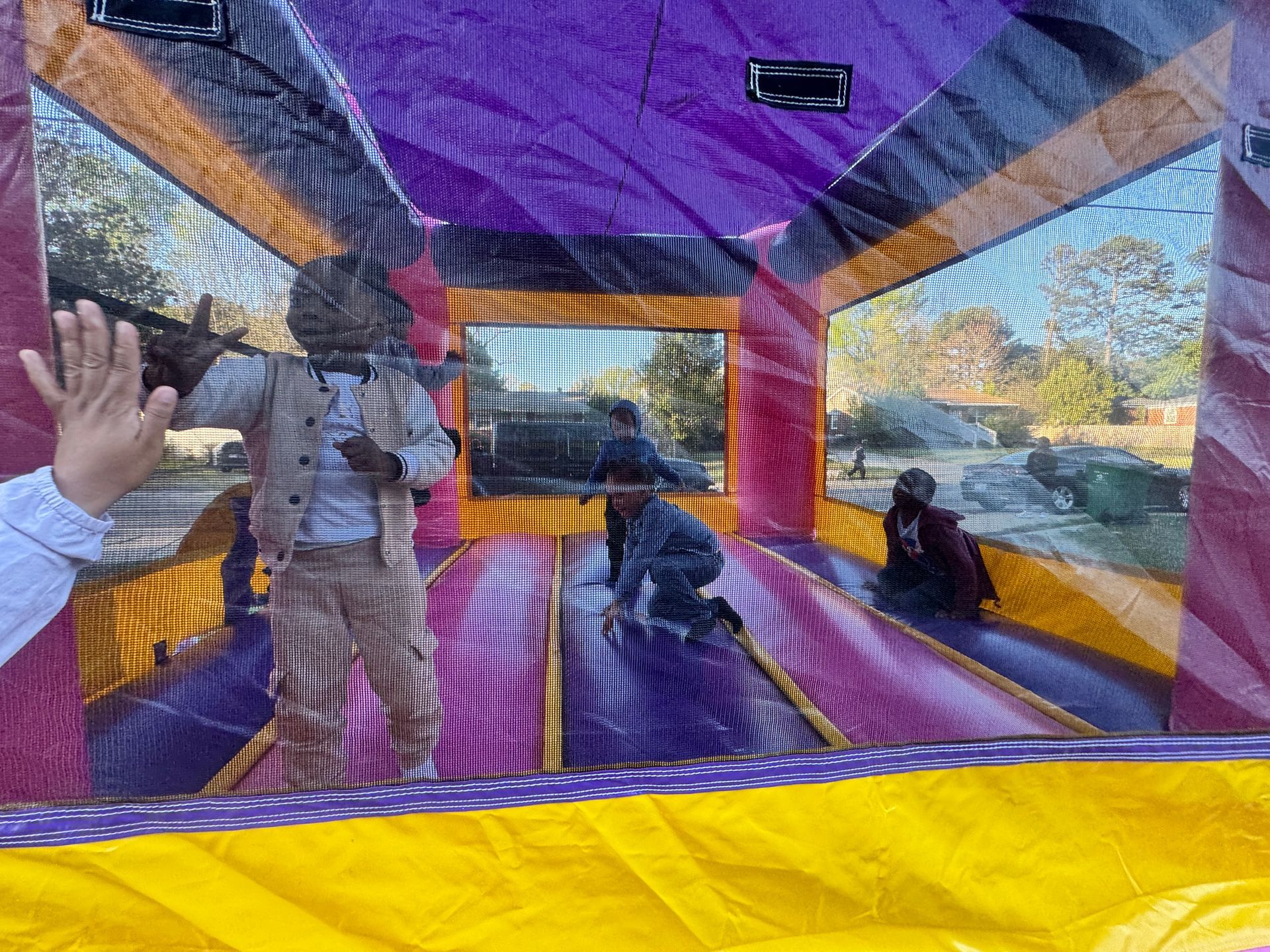 Three children playing inside a purple, yellow, and orange inflatable bounce house.