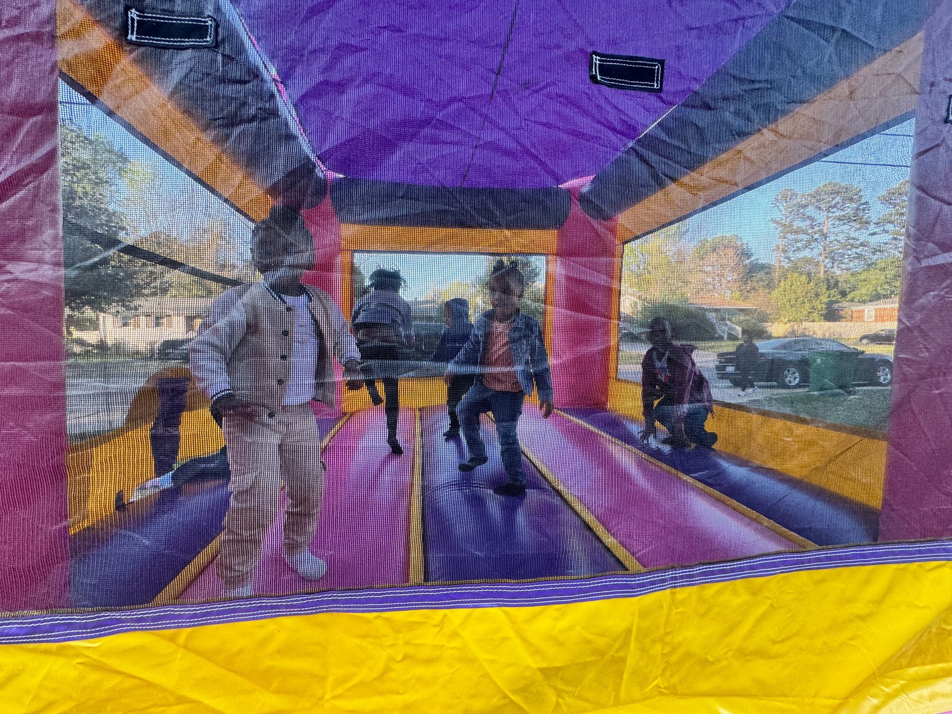 Children jump inside a purple and yellow inflatable bounce house on a sunny day.