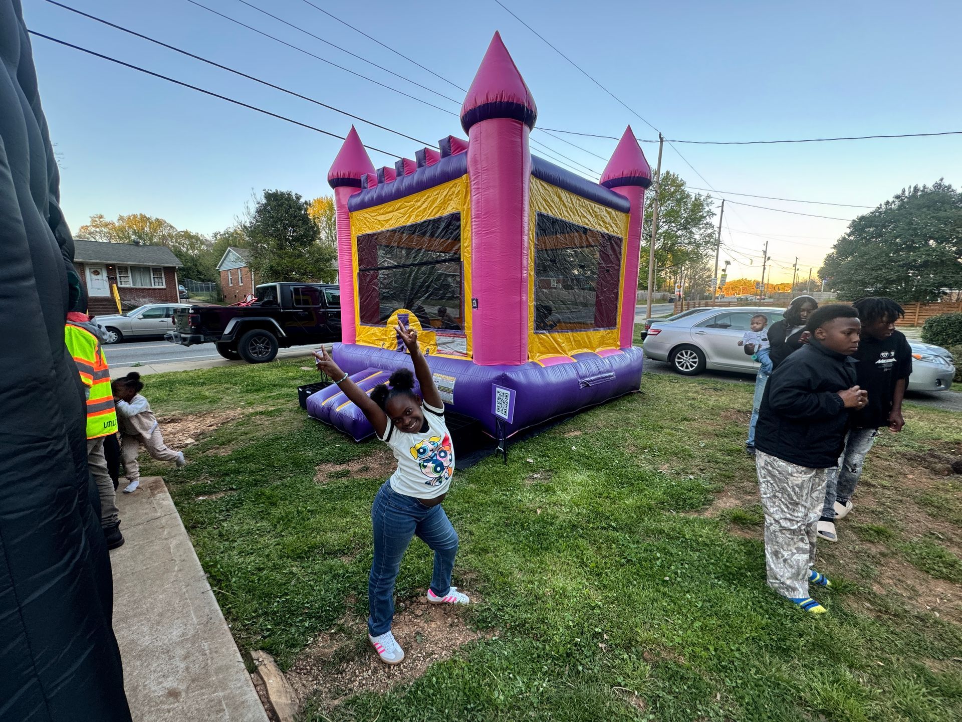 A child poses in front of a bright pink and yellow bouncy castle set up in a residential yard.