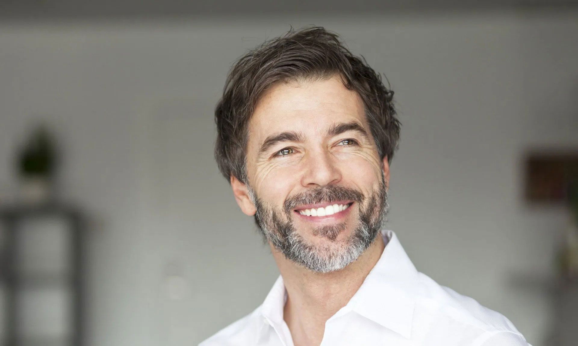 A man with a beard is smiling and wearing a white shirt.