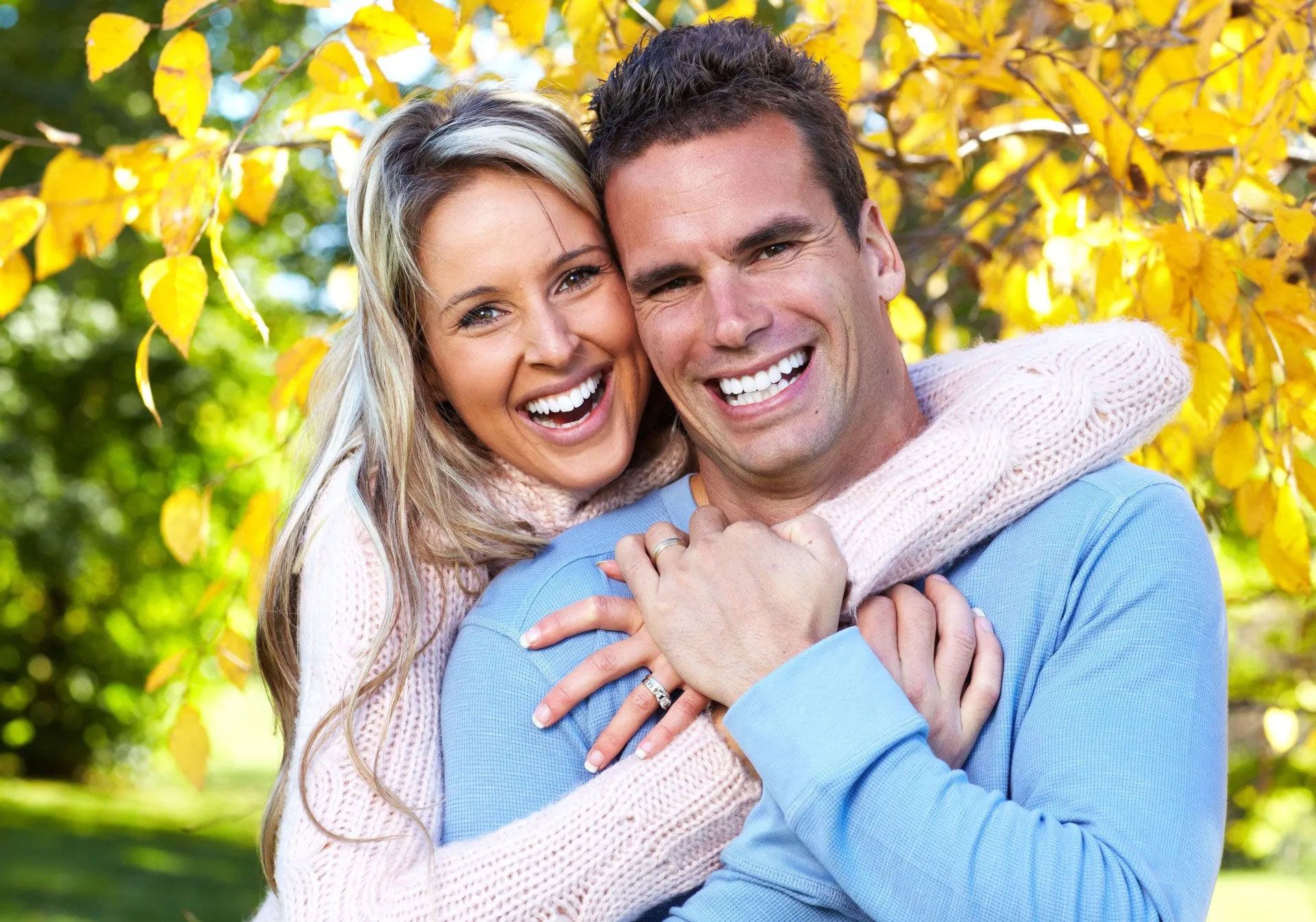 A man and a woman are hugging each other in a park.