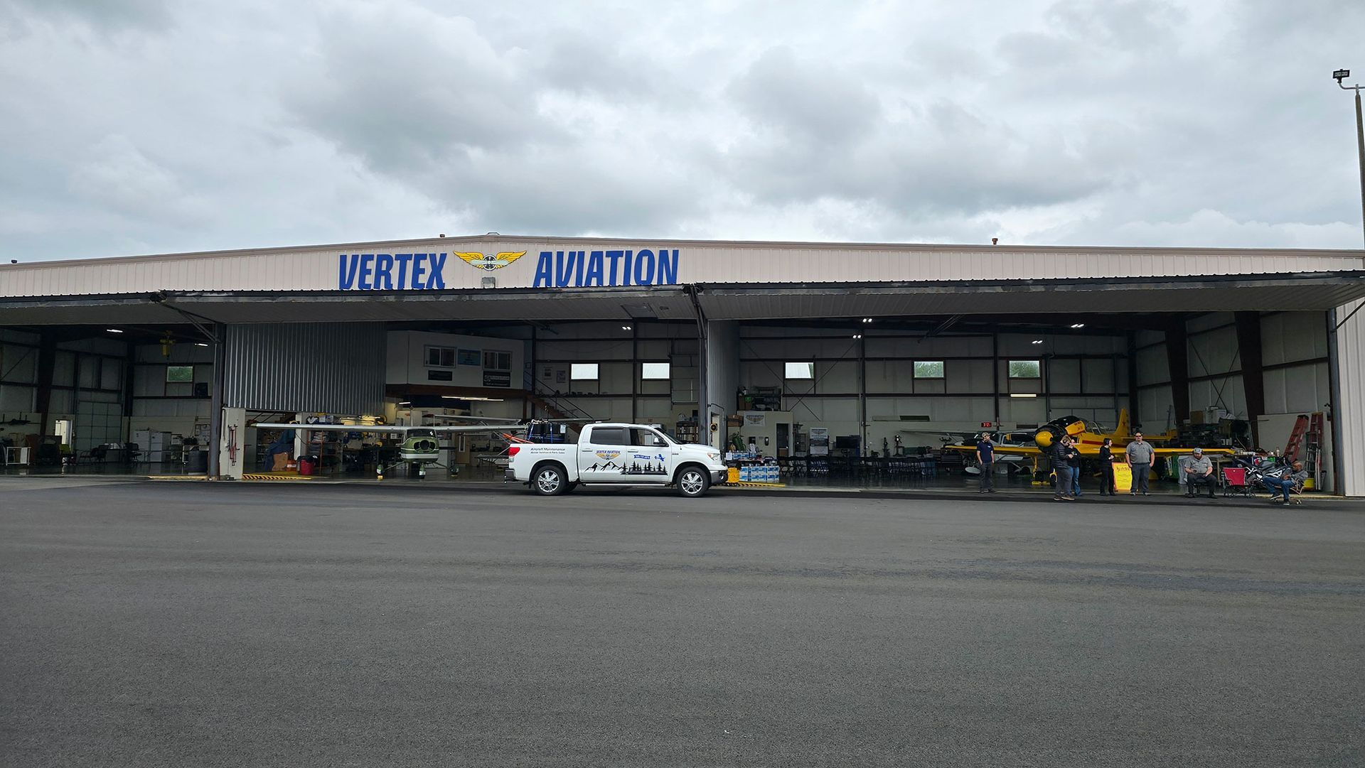 Vortex Aviation hangar with a white truck parked in front. Overcast sky.