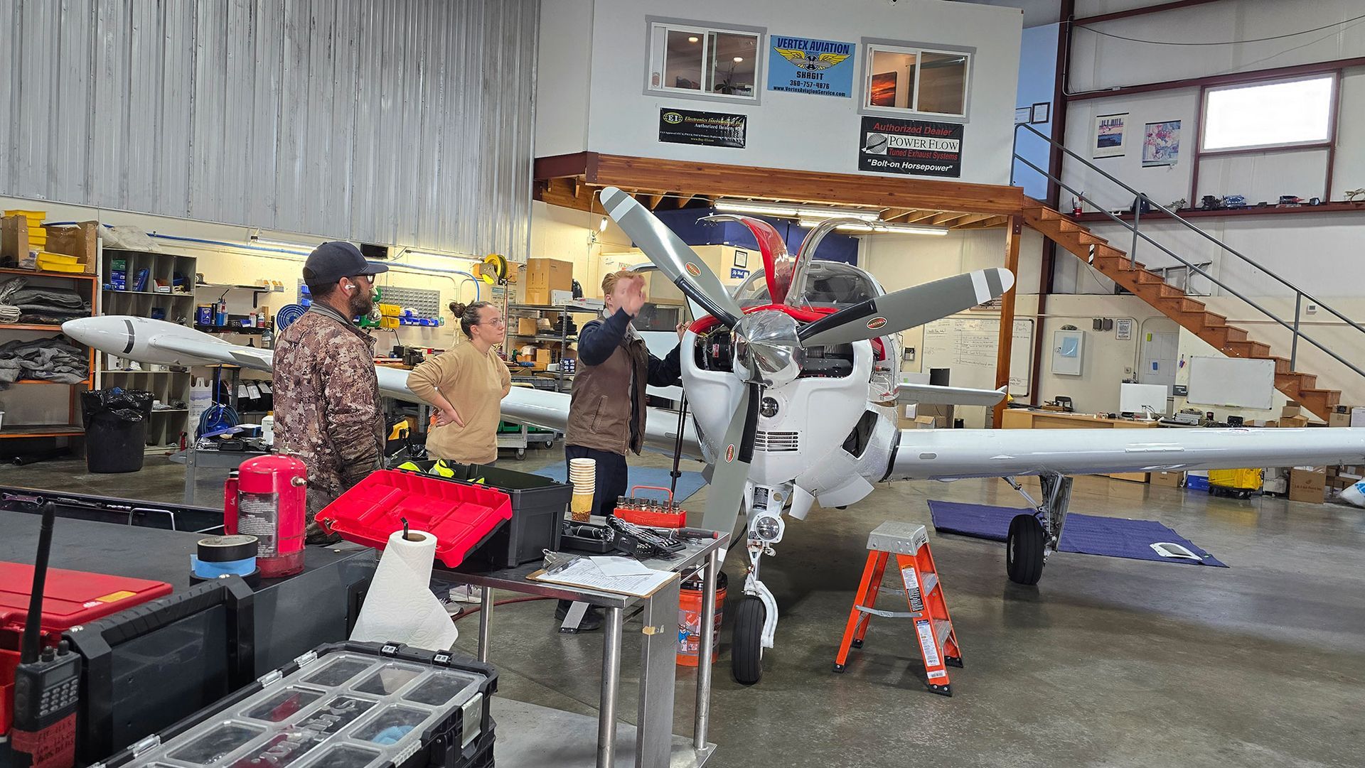People working on an airplane in a hangar. They are inspecting the propeller and engine.