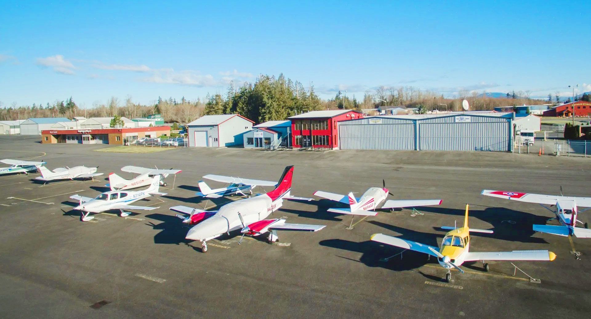 Airplanes parked on a tarmac in front of hangars on a sunny day.