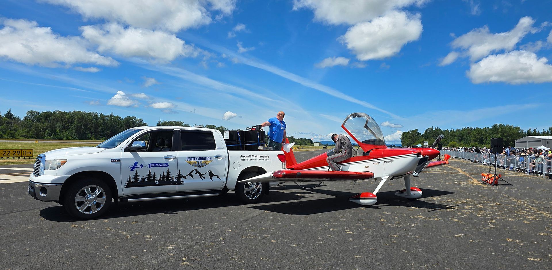 White truck with plane attached, parked on tarmac under blue sky.