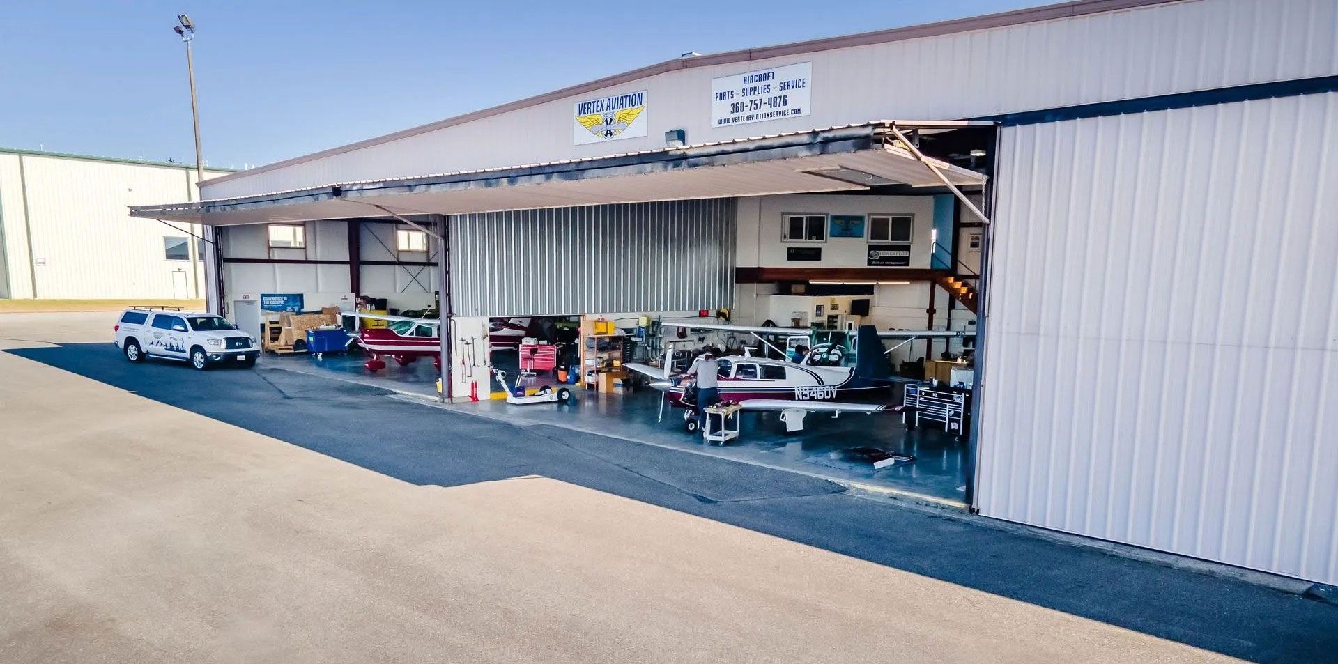 Aircraft hangar with several vehicles inside, white truck on the left.