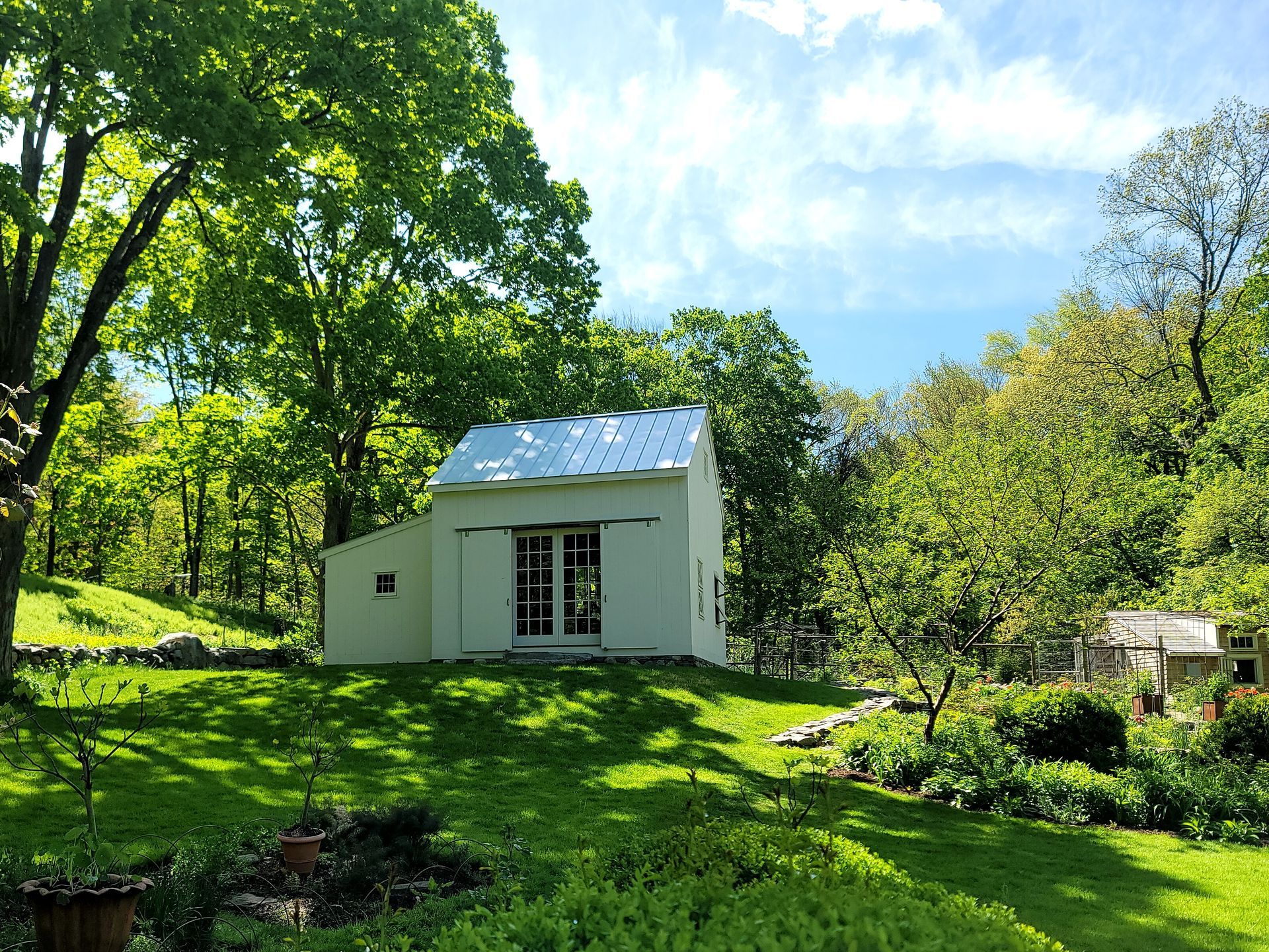 A small white house is sitting in the middle of a lush green field surrounded by trees.