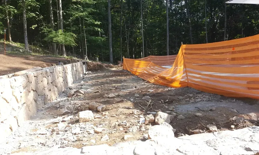 A construction site with a fence and trees in the background.