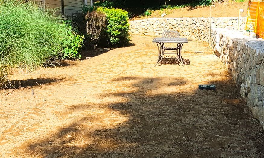 A table and chairs are sitting in a dirt yard next to a stone wall.