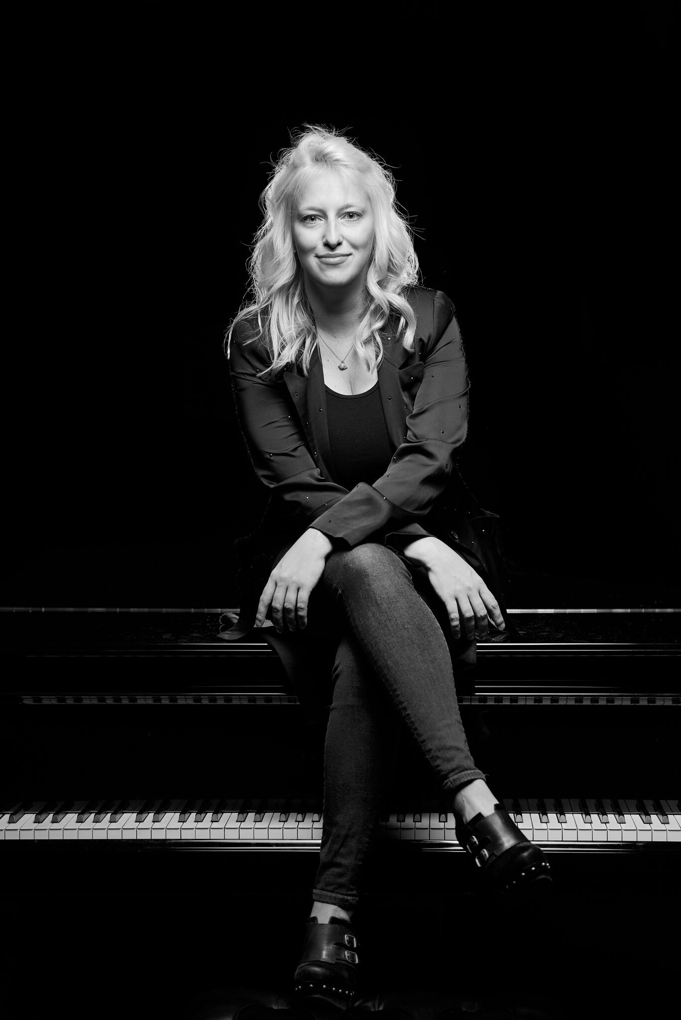 A woman is sitting on a piano in a black and white photo.