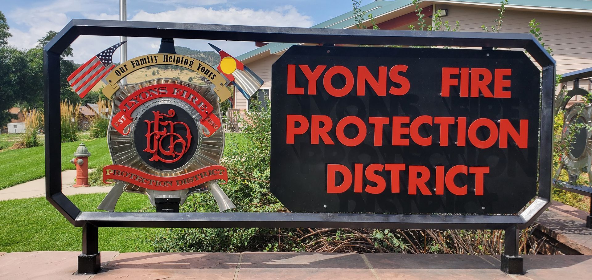A metal sign for the Lyons Fire Protection District with a department emblem, an American flag, and the Colorado flag.