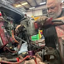 A man is working on a car with a drill in a garage.