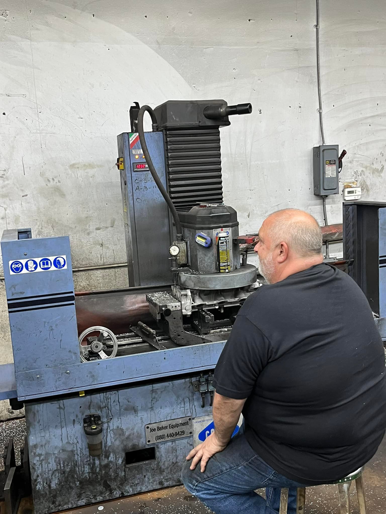 A man is kneeling down in front of a machine in a garage.