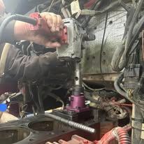 A man is working on a truck engine with a drill.