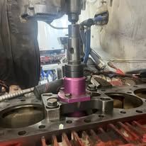 A person is using a machine to cut a hole in a cylinder head.