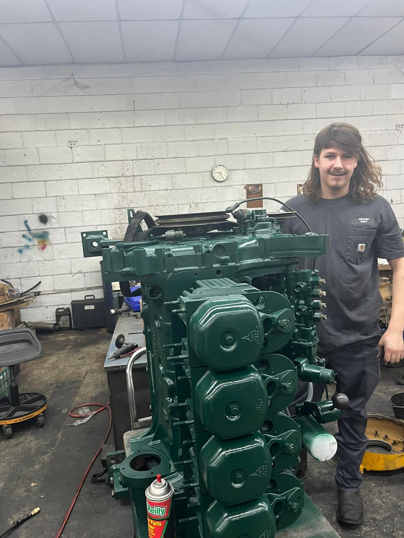 A man is standing in front of a large green engine in a garage.