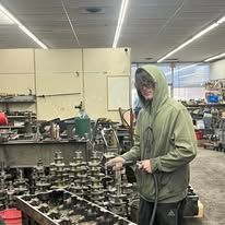 A man in a green hoodie is working on a machine in a factory.