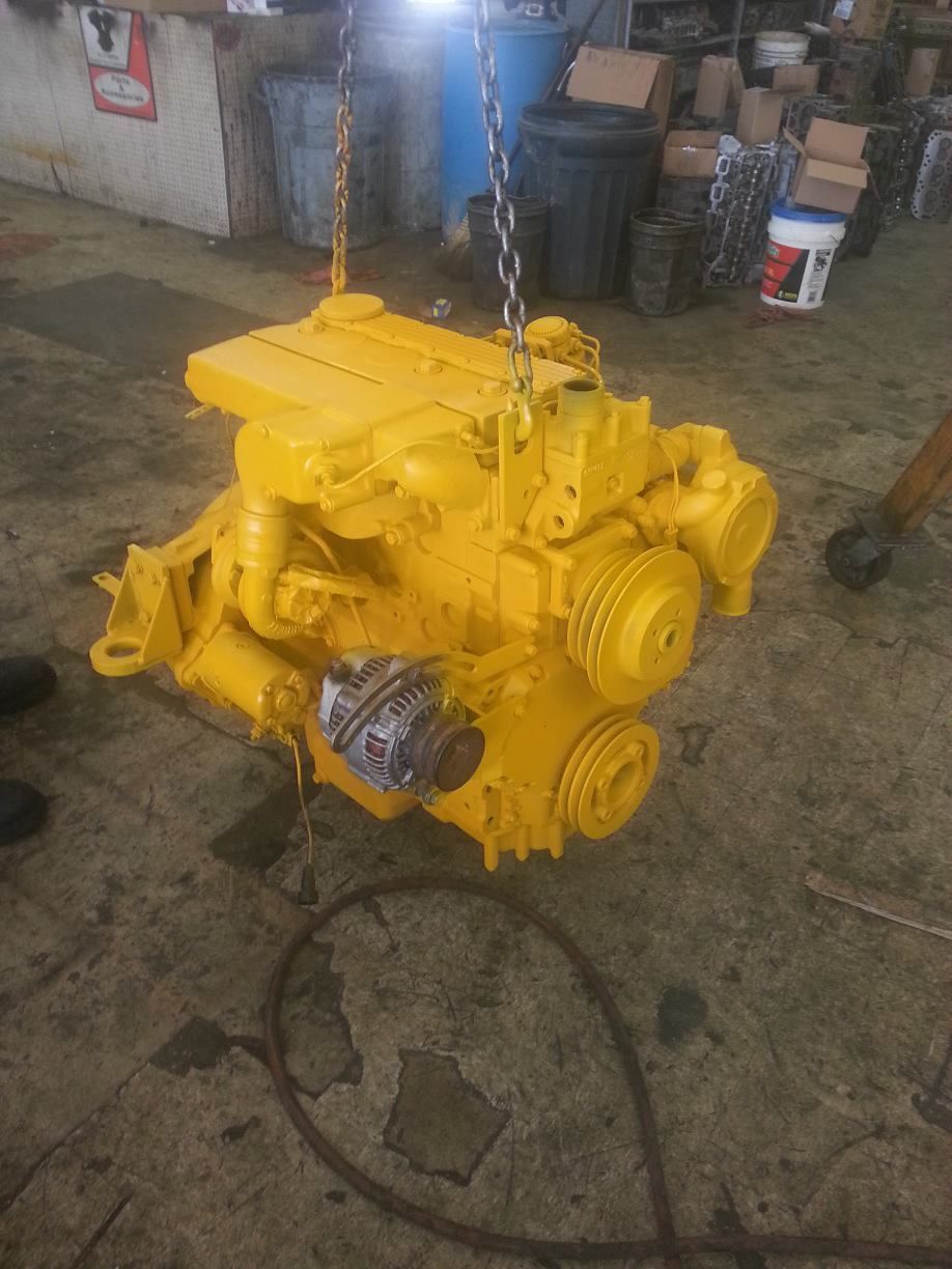 A yellow engine is hanging from chains in a garage.