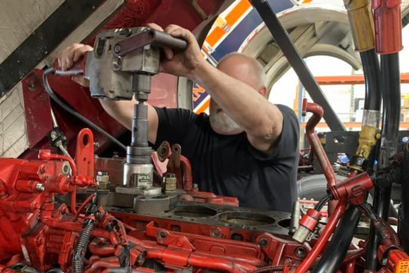 A man is working on a red engine with a wrench