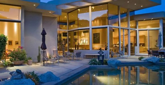 Modern hotel courtyard with a lit pool, lounge chairs, and large glass windows at dusk