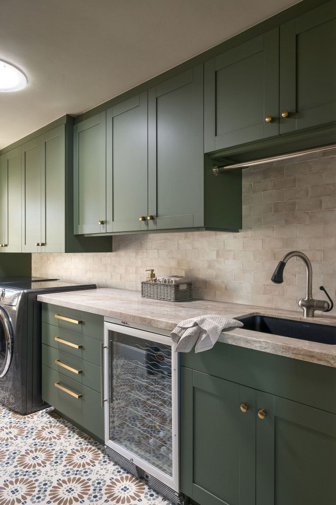 Green kitchen cabinets with black countertop, sink, patterned tile floor, and washer/dryer under the counter.