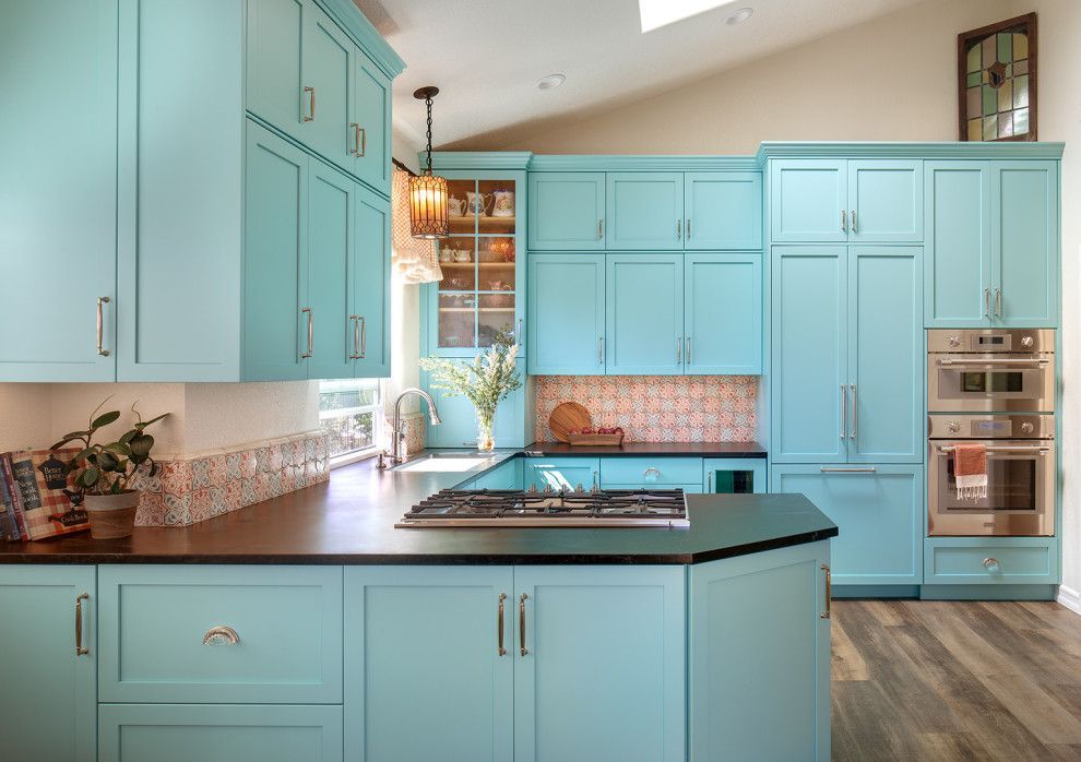 Bright turquoise kitchen with island, black countertops, and stainless steel ovens