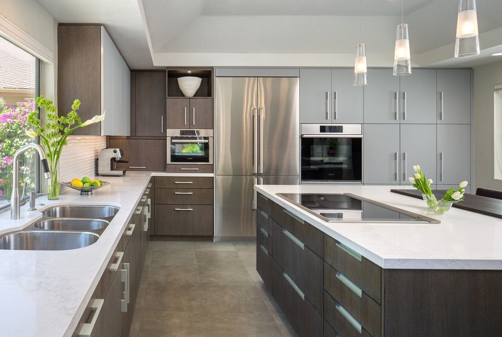 Modern kitchen with stainless steel appliances, gray cabinets, and white countertops with a central island.