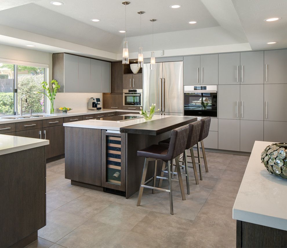 Modern gray kitchen with island, bar stools, stainless appliances, and large window overlooking greenery