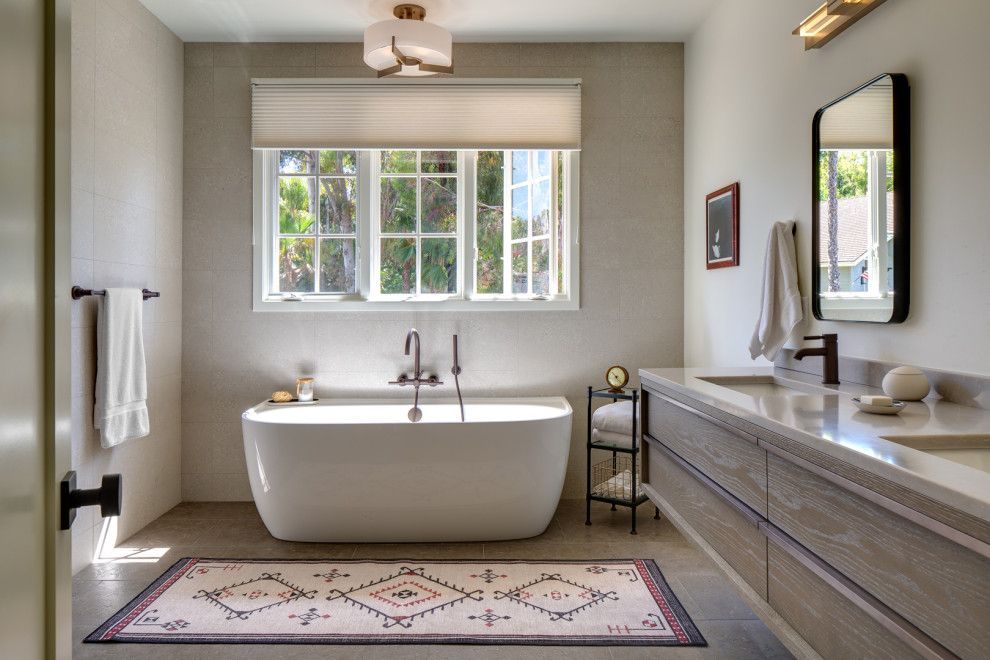 Modern bathroom with freestanding tub, double vanity, window, and patterned rug