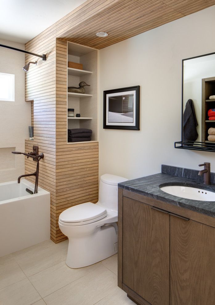 Modern bathroom with toilet, sink, bathtub, and built-in shelving in neutral tones