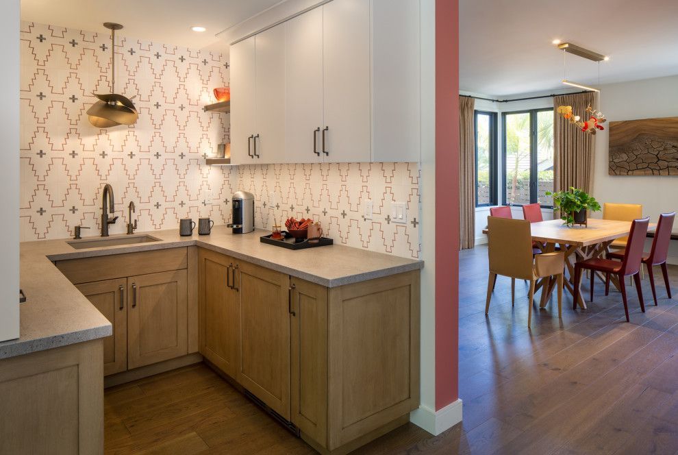 Modern kitchen opening to dining area, with wood cabinets, white patterned backsplash, and table by large windows