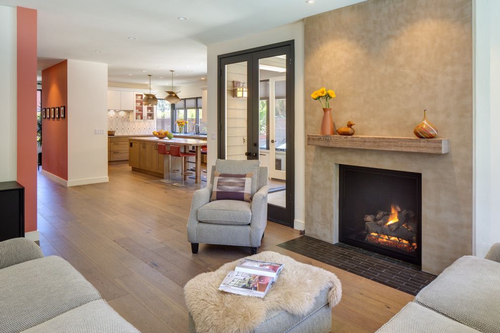 Modern living room with fireplace, gray chairs, wood floors, and an open kitchen area