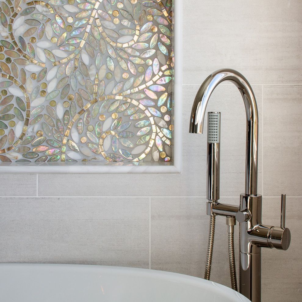 Chrome handheld showerhead beside frosted tile wall and iridescent mosaic panel