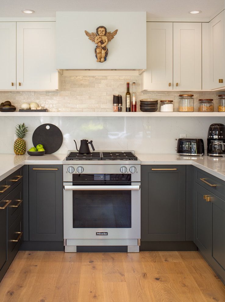 Modern kitchen with dark cabinets, stainless steel oven, white backsplash, and wooden floor