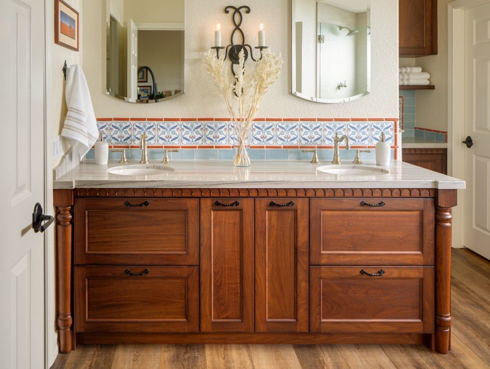 Bathroom vanity with wood cabinets, dual sinks, and a large mirror above a patterned tile backsplash