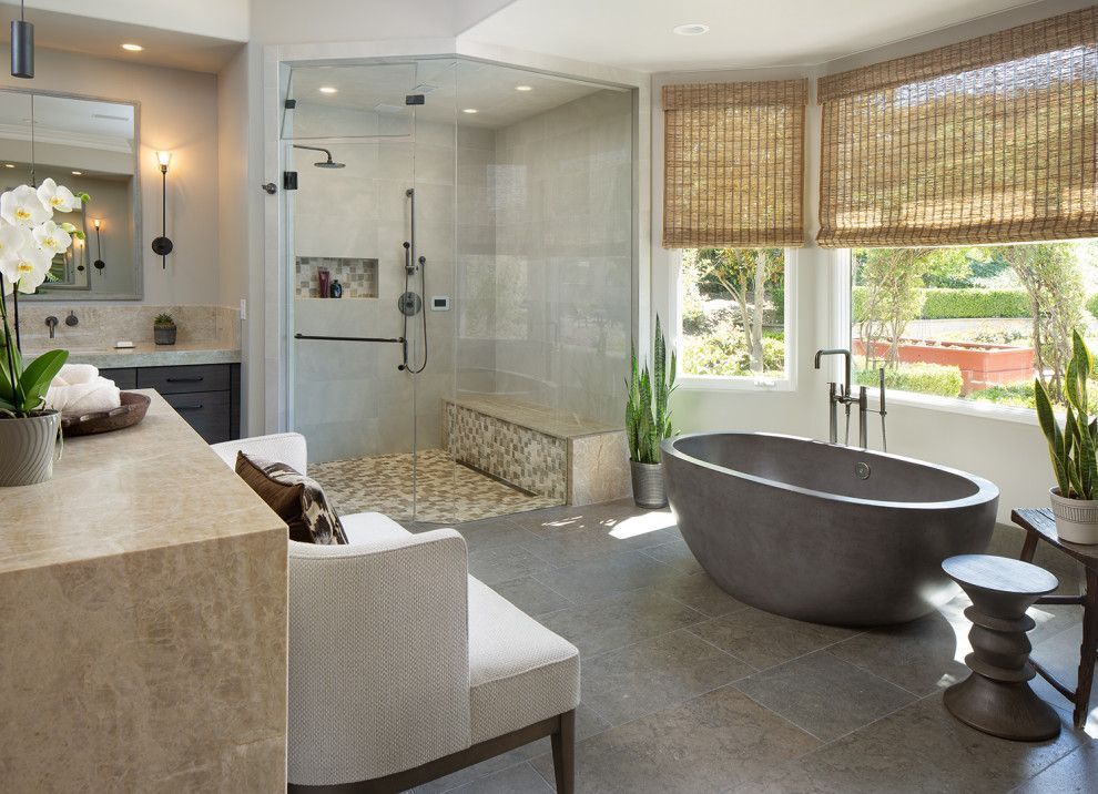 Modern bathroom with glass shower, freestanding tub, vanity, and woven window shades.