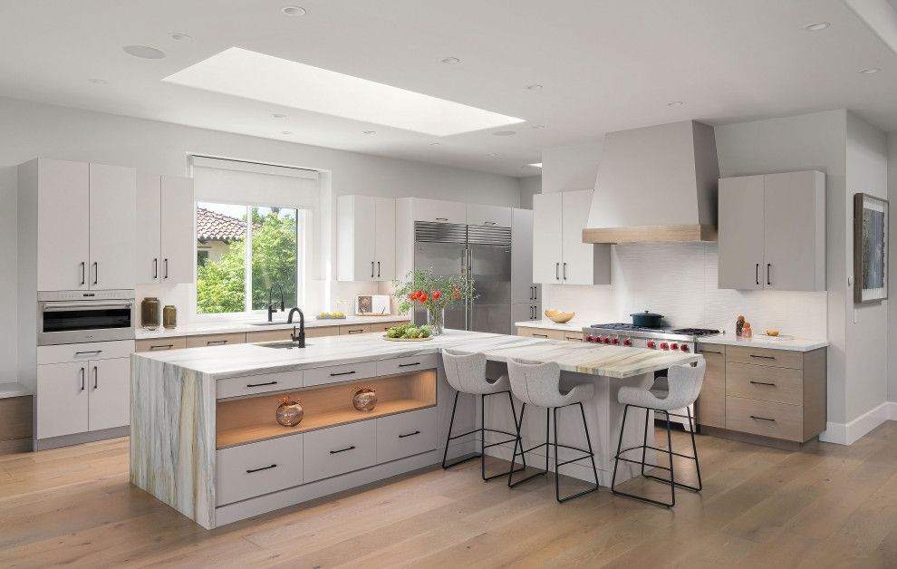 Bright modern kitchen with white cabinets, island, dining table, and wood floors.