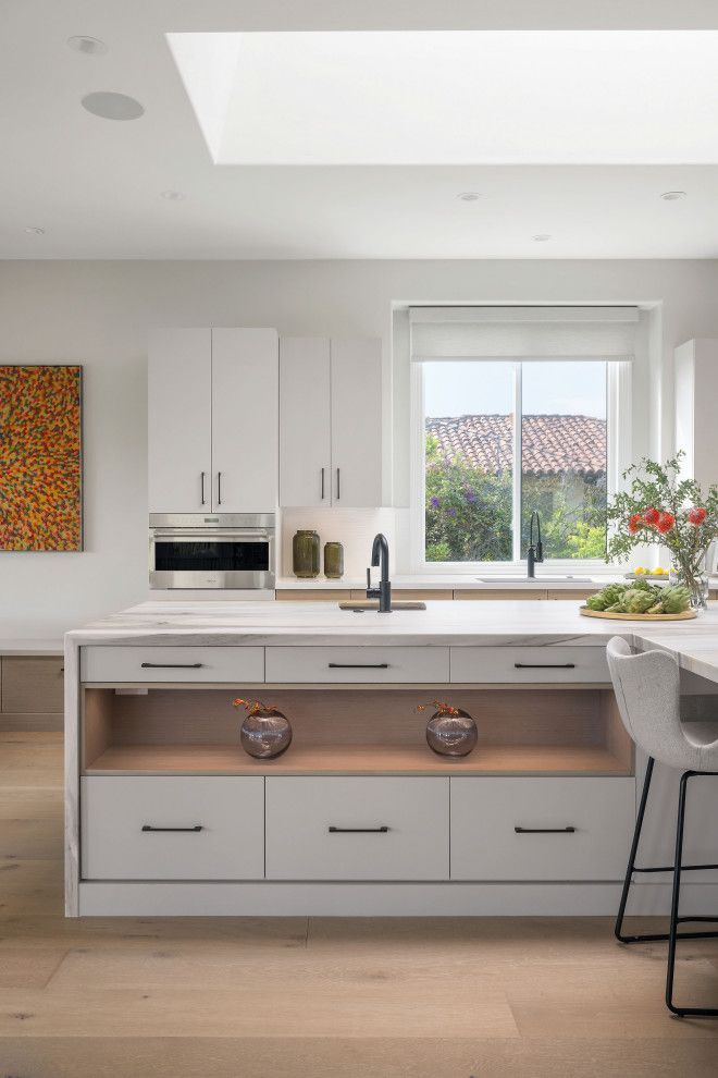 Bright modern kitchen with white cabinets, island sink, skylight, and a bowl of flowers by the window