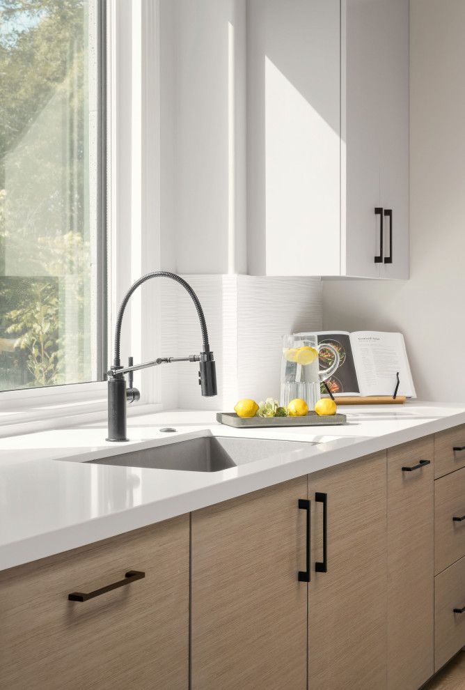 Modern kitchen sink by a window with a chrome faucet, white cabinets, and a bowl of lemons on the counter