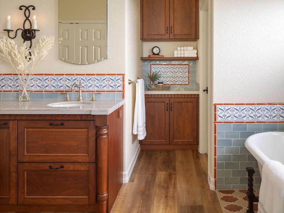Warm bathroom with wood vanity, blue tile trim, sink, tub, and towel by a built-in cabinet.