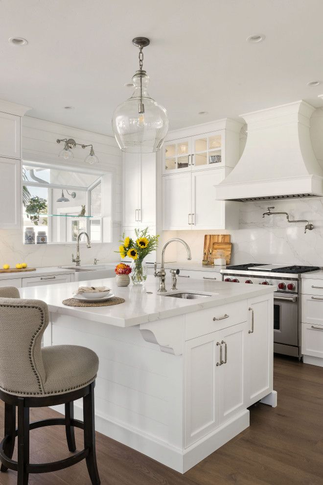 Bright white kitchen with island, bar stools, gas range, and a vase of flowers near a sunny window