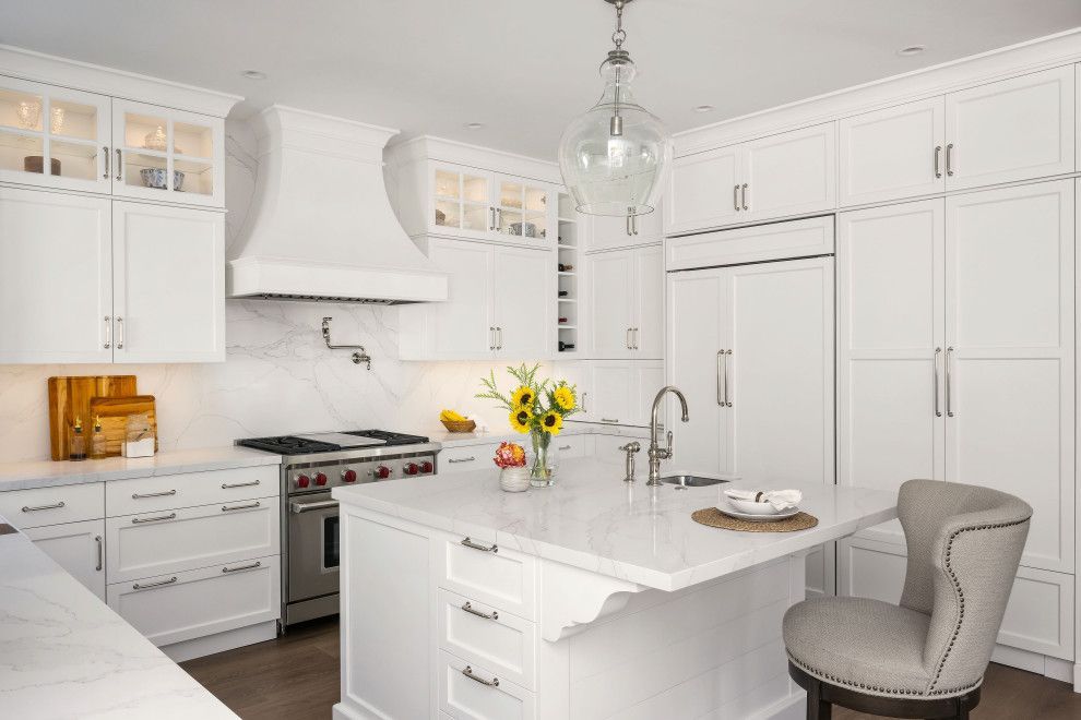Bright white modern kitchen with island, stainless stove, large refrigerator, and a vase of yellow flowers.