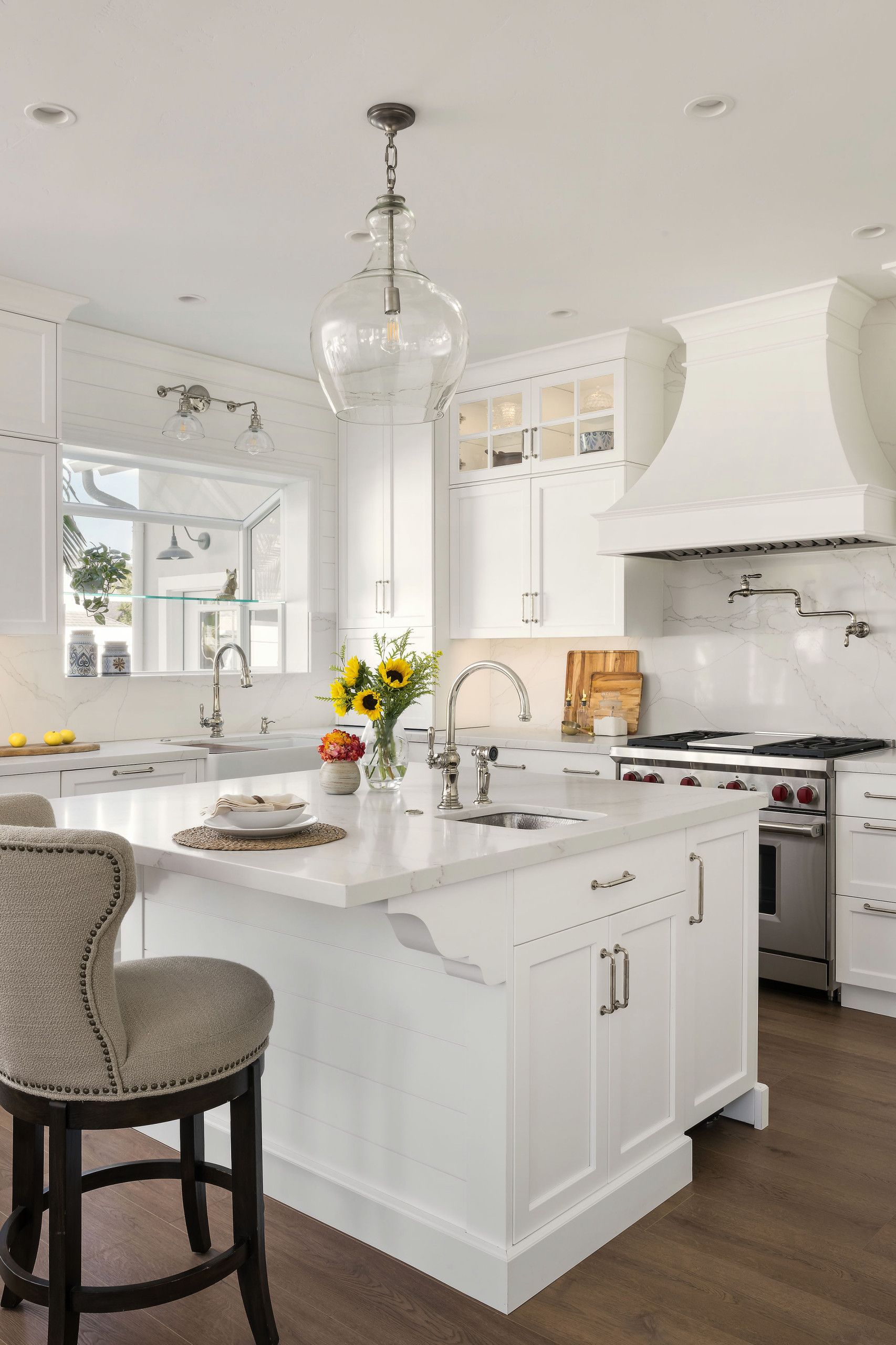 Bright white kitchen with a marble island, barstool, flowers, and stainless-steel stove