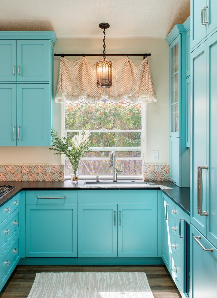 Turquoise kitchen with white countertops, window, and patterned valance above the sink.
