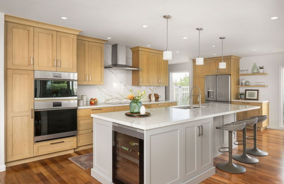 Bright modern kitchen with light wood cabinets, white island, stainless steel appliances, and bar stools