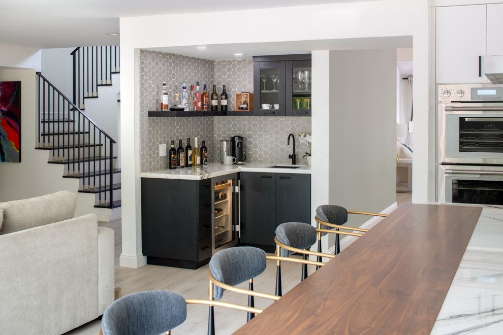 Modern kitchen with a small bar, dark cabinets, and stools beside a wooden island tabletop.
