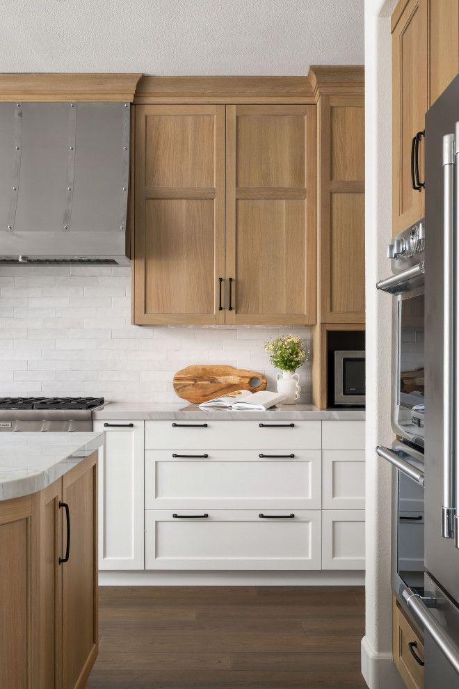 Modern kitchen with wood cabinets, white drawers, stainless fridge, and a countertop holding flowers and bread.