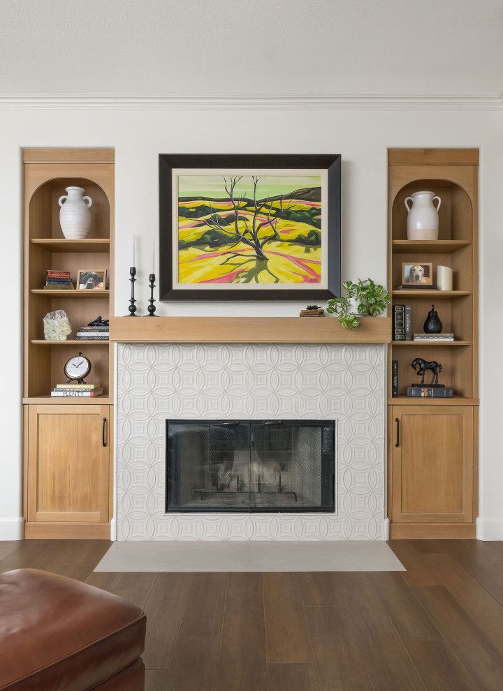Living room fireplace with built-in shelves, artwork above the mantel, and a leather chair in the foreground
